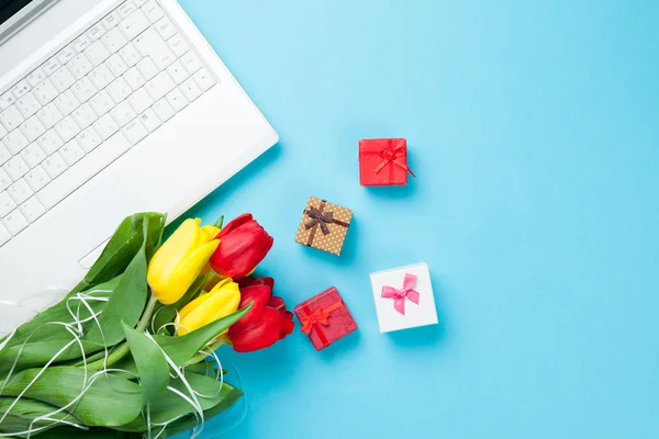 Bílý počítač a kytice tulipánů s dárky — Stock fotografie