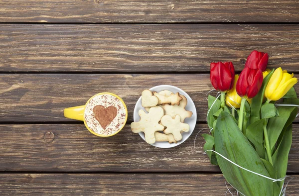 Xícara de cappuccino com forma de coração e buquê de tulipas com co — Fotografia de Stock