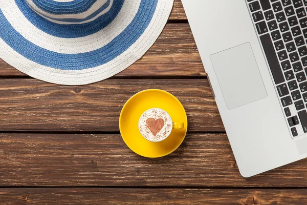 Tasse Cappuccino und Hut neben Laptop — Stockfoto