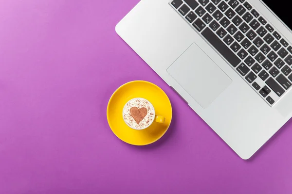 Cup of cappuccino with heart shape and laptop