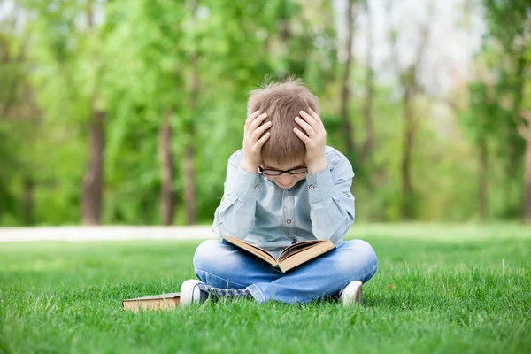 Sad boy with book on green grass — Stock Photo, Image