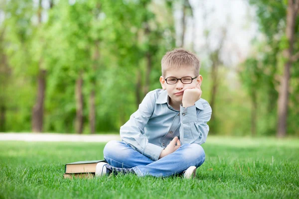 Smutny chłopiec z książki na zielonej trawie — Zdjęcie stockowe
