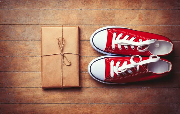 Red gumshoes and package on wooden table. — Stock Photo, Image