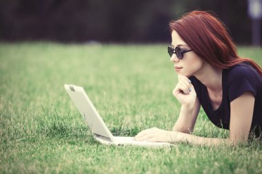 Redhaired Woman on meadow with laptop