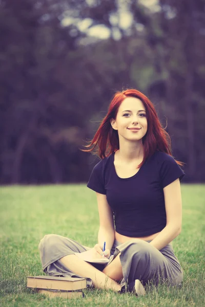 Redhaired Woman sitting studying on meadow — Stockfoto
