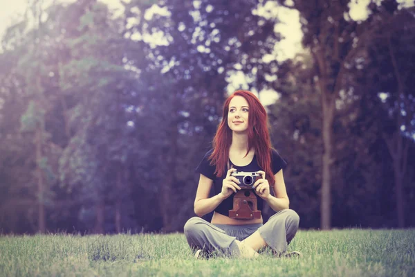 Рудоволоса жінка з камерою сидить на траві — стокове фото