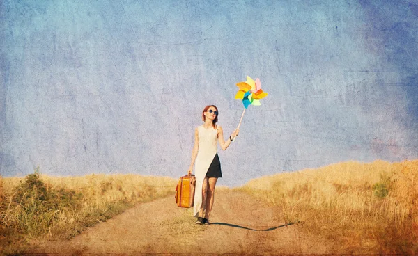 Girl with suitcase and wind toy at countryside — Stockfoto