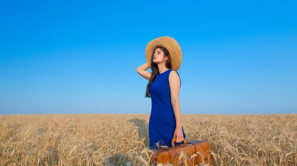 Девушка с чемоданом на пшеничном поле — стоковое фото