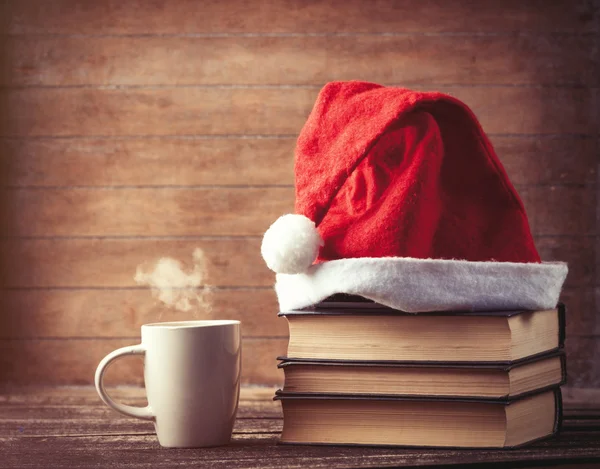 Mikołaje kapelusz nad książkami w pobliżu gorący kubek — Zdjęcie stockowe