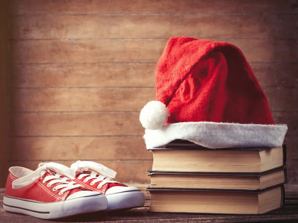 Sombrero de Santas sobre libros cerca de zapatos de goma rojos —  Fotos de Stock