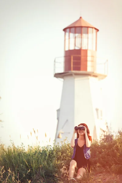 Girl with binocular sitting on the grass near Lighthouse — Stock Photo, Image