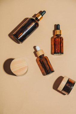 Koyu cam krem kavanoz ve kozmetik sıvısı kabı yumuşak bej arka planda düzenlenmiş ve minimalist bir cilt bakımı konsepti yaratıyor.