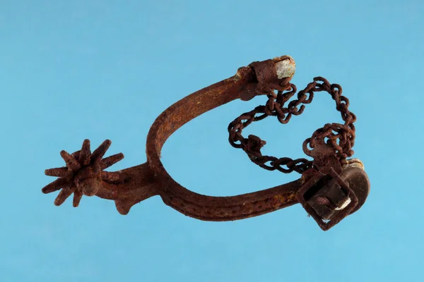 Old and rusty riding spur on blue background — Stock Photo, Image