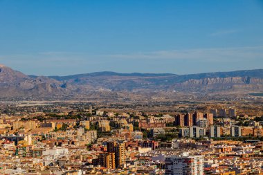 Geniş bir şehir, berrak mavi gökyüzünün altındaki uzak dağlara doğru uzanıyor.. 