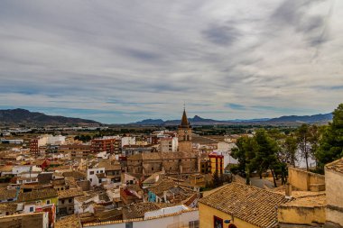 İspanya 'nın Villena şehrinde geniş bulut dolu gökyüzünün altında taşralı tuğlalı evler yayılıyor.