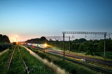 Akşamları tren arka planında hareket ederken ışıkları açık bir yük treni.