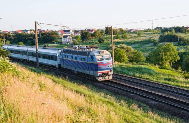 Kırsal kesimin arka planında demiryolunda hareket ederken arabalı yolcu treni