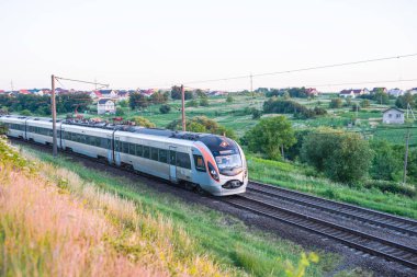 Kırsal kesimin arka planında demiryolunda hareket ederken arabalı yolcu treni