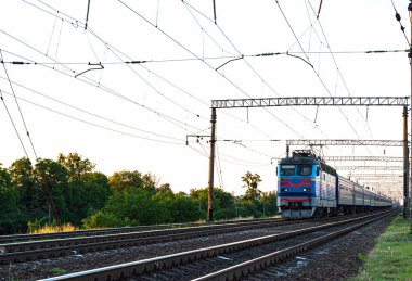 Kırsal kesimin arka planında demiryolunda hareket ederken arabalı yolcu treni