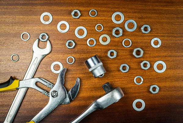 Adjustable, ratchet wrench and open-end wrenches with nuts and washers on a brown wood texture background