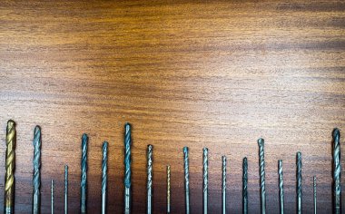 Ahşap ve metali delmek için farklı çaplı matkaplar kahverengi ahşap dokunun arka planında bir sırada sergilenmektedir.