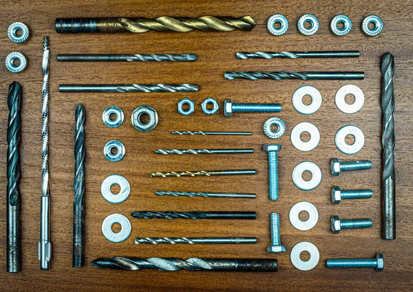 Düğüm stili fotoğraf - kahverengi ahşap dokunun arka planında çeşitli cıvatalar, fındıklar, matkaplar ve makineler mekanik onarım için