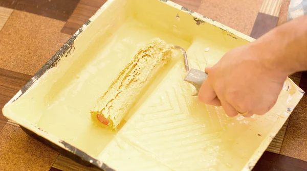 The process of soaking the roller in a container with a yellow — Stock Photo, Image