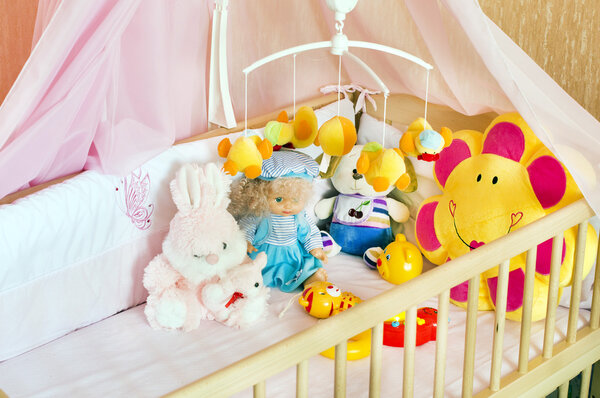 Различные мягкие игрушки в детской кроватке с оранжевым бельем
 