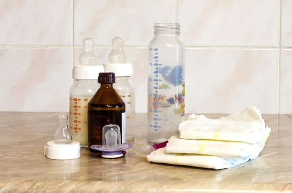 Different glass bottles with a mixture of feeding and baby diape — Stock Photo, Image