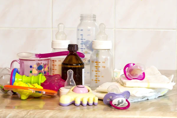 Biberón de vidrio con la mezcla para la alimentación, juguetes y pañales para bebés —  Fotos de Stock