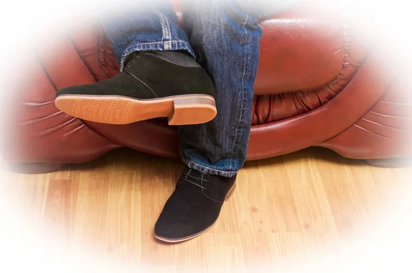 Un hombre en jeans y zapatos en un sofá de cuero — Foto de Stock