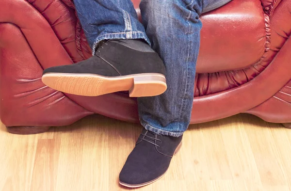 Мужчина в джинсах и туфлях на кожаном диване — стоковое фото
