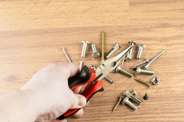 Pliers in hand on a background of various bolts — Stock Photo, Image
