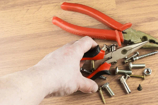 Pliers in hand on a background of various bolts and dowels — Stock Photo, Image