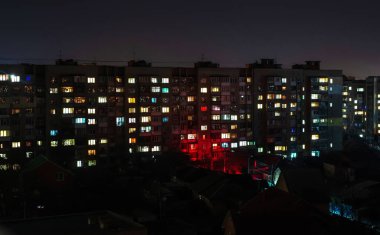 Büyük bir şehirde gece yarısı pencereleri açık olan bir apartman.