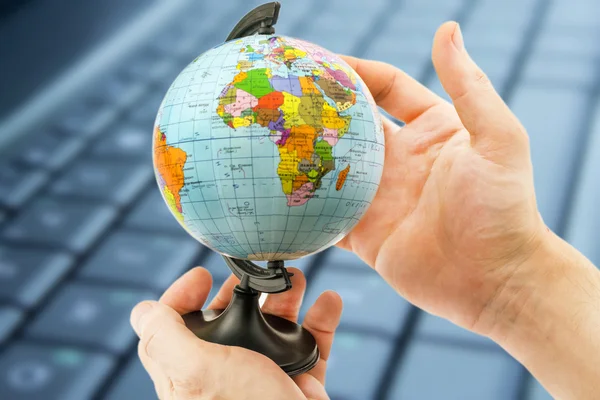 Globe in hand against the background of the keyboard