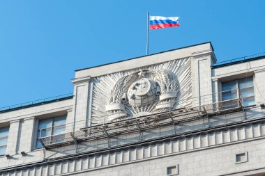 Moskova 'daki Duma Devlet Binası' nın duvarında asılı olan Sovyet arması aynı zamanda Gosduma olarak da bilinir. Rus Ulusal Bayrağı binanın tepesinde dalgalanıyor. Açık mavi gökyüzü.