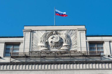 Moskova 'daki Duma Devlet Binası' nın duvarında asılı olan Sovyet arması aynı zamanda Gosduma olarak da bilinir. Rus Ulusal Bayrağı binanın tepesinde dalgalanıyor. Açık mavi gökyüzü.