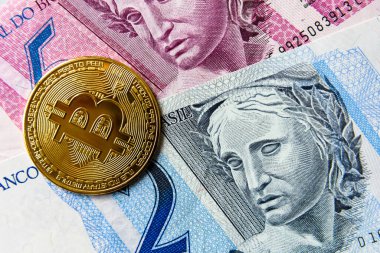 Elektronik altın Bitcoin madeni para ve arkasında da Brezilyalı bir gerçek. Brezilya gerçeğinin merkezi olmayan para birimine karşı devalüasyonu.