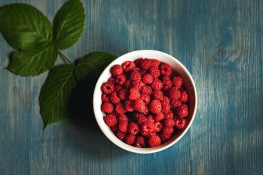 Mavi ahşap masada kasede taze ahududu. Üst görünüm.