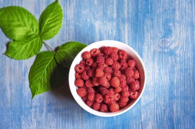 Mavi ahşap masada kasede taze ahududu. Üst görünüm.