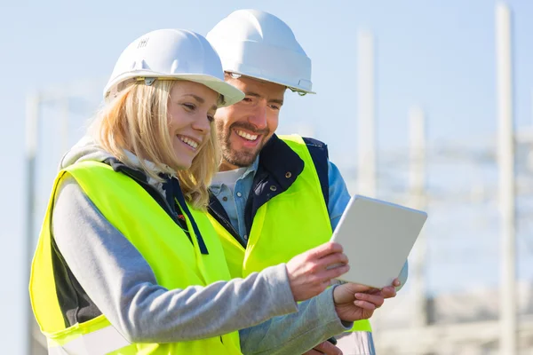 Dos trabajadores que trabajan fuera con una tableta en un sitio de construcción — Foto de Stock