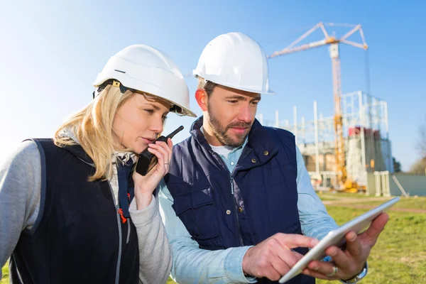 Dos trabajadores que trabajan fuera con una tableta en un sitio de construcción — Foto de Stock