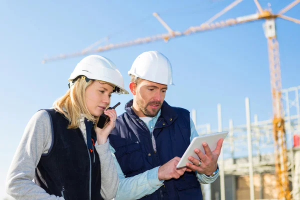 Dos trabajadores que trabajan fuera con una tableta en un sitio de construcción — Foto de Stock