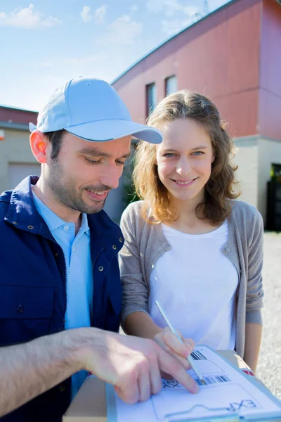 Young attractive woman signing on delivery paper — Stock Photo, Image