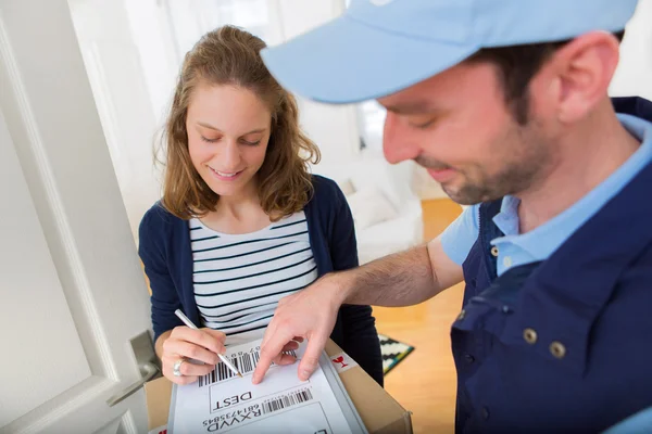 Young attractive woman signing on delivery paper — Stock Photo, Image