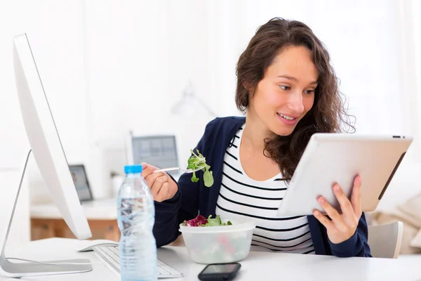 Jovem estudante atraente comendo salada enquanto usa tablet — Fotografia de Stock