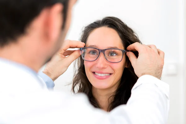 Jonge aantrekkelijke vrouw probeert bril w opticien — Stockfoto