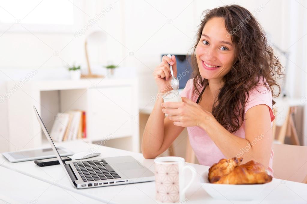 Young attractive student taking breakfast while working