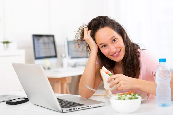 Young attractive student  eating sandwich while working — Stock Photo, Image